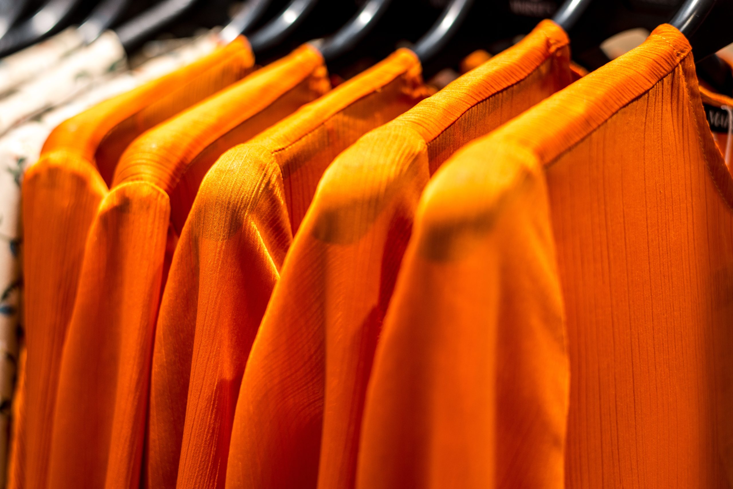 Close-up of orange garments hanging on black hangers.