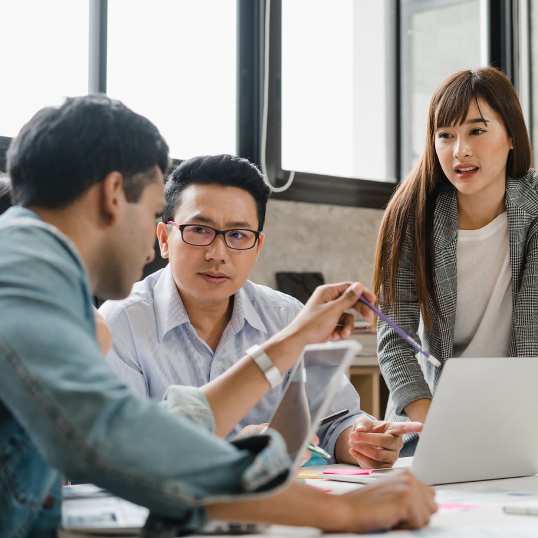A group of four people having a discussion around a table with laptops in an office setting.