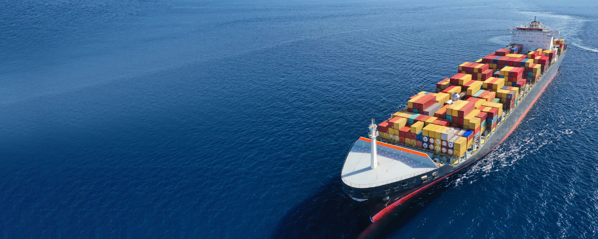 Aerial view of a cargo ship with colorful containers sailing on a blue ocean.