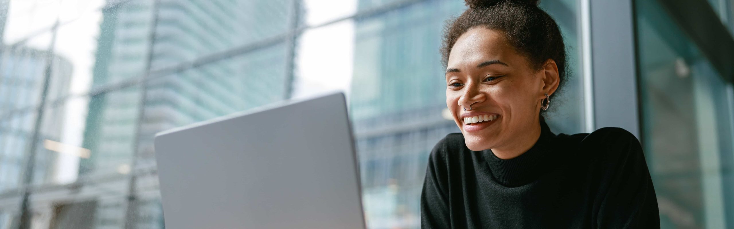 Person smiling at a laptop with cityscape in the background.