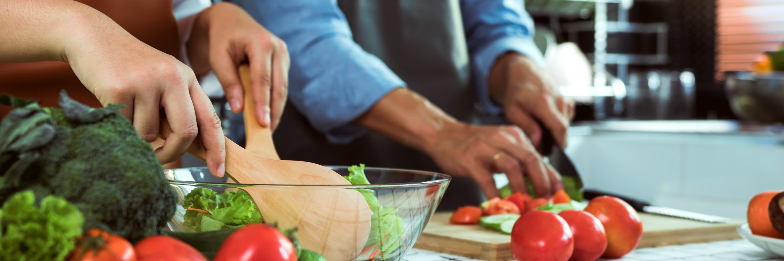 People preparing a salad and slicing vegetables in a kitchen.