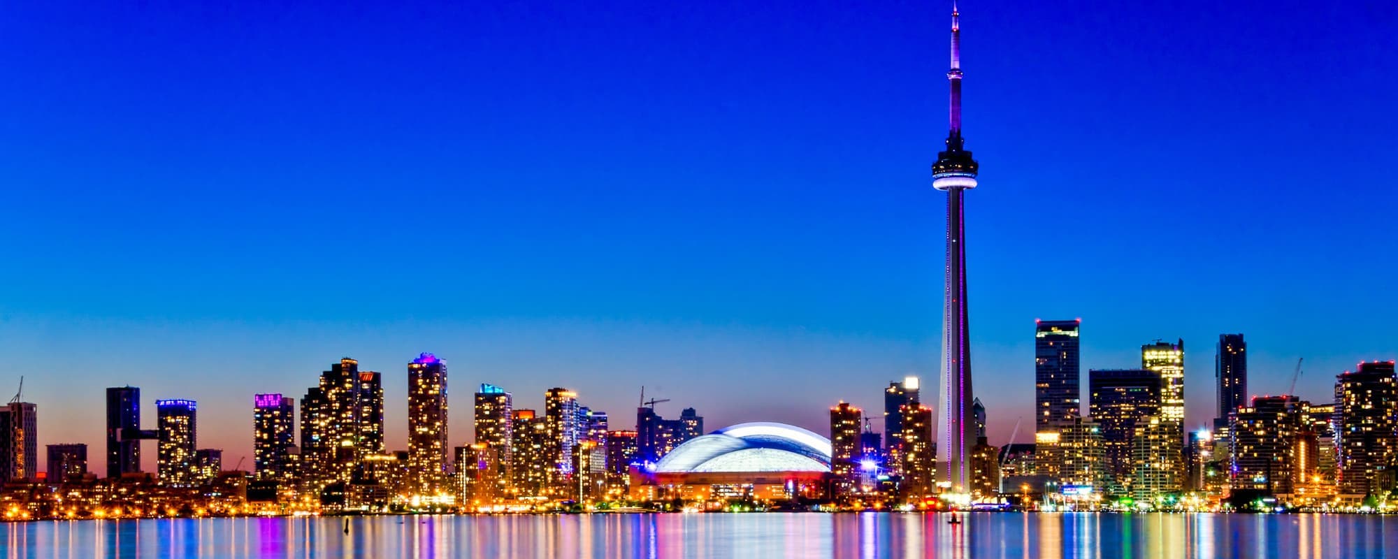 City skyline at dusk with lit buildings reflected on water.