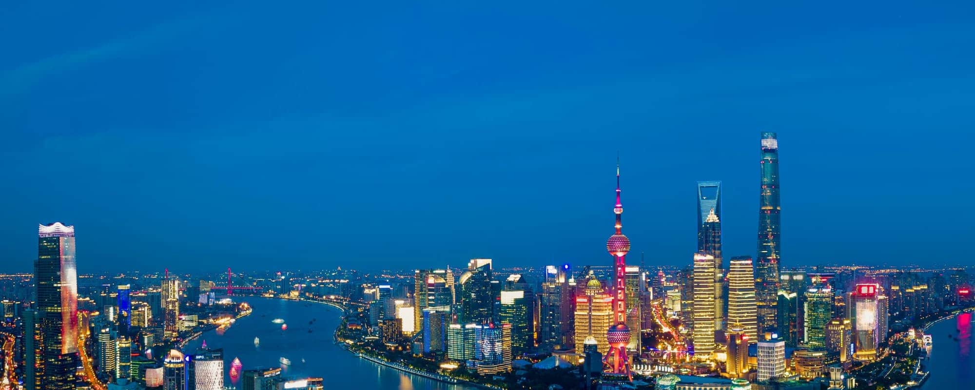 Panoramic view of a city skyline at night with illuminated skyscrapers and a river.