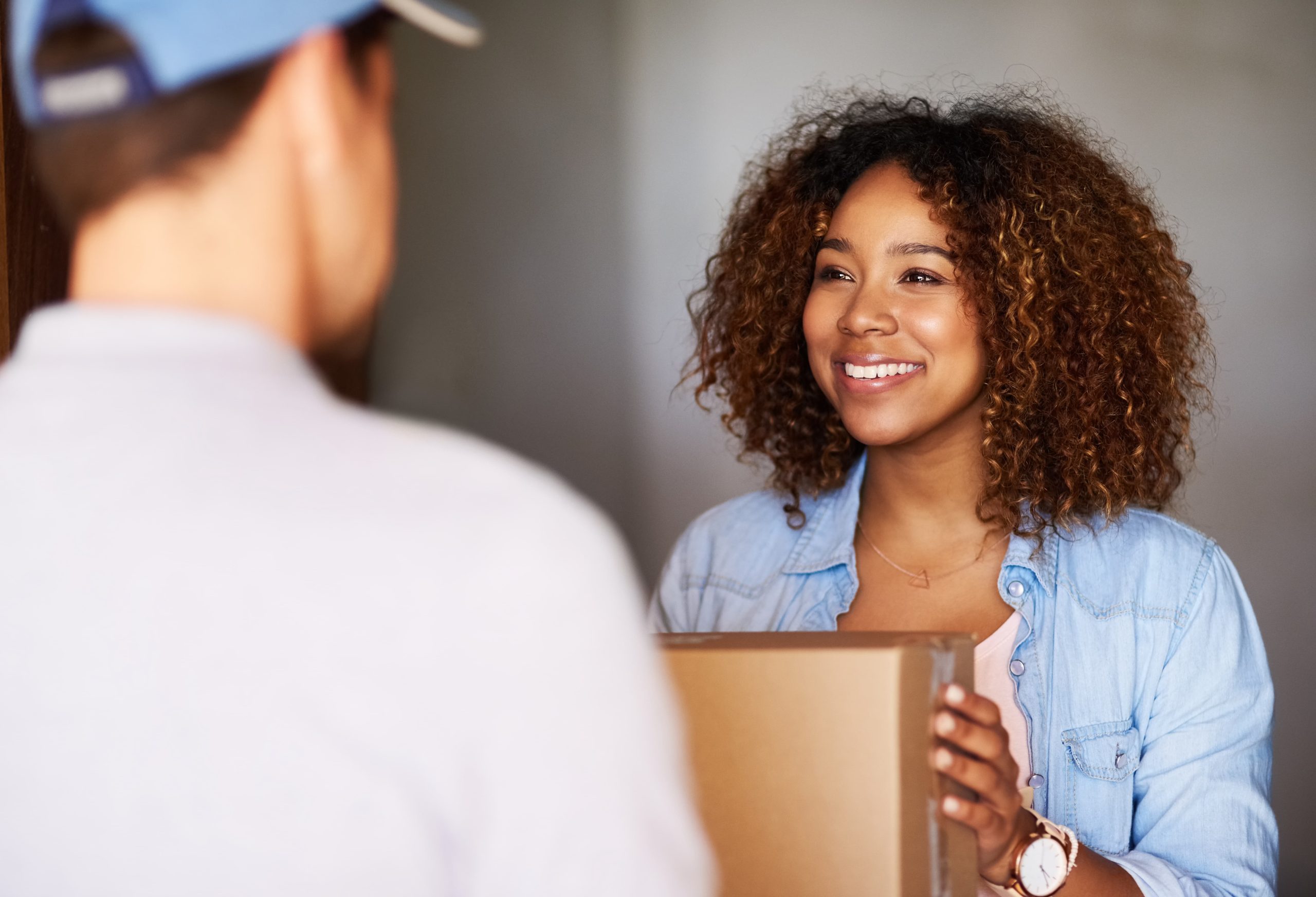 A woman smiling while receiving a package from a delivery person indoors.