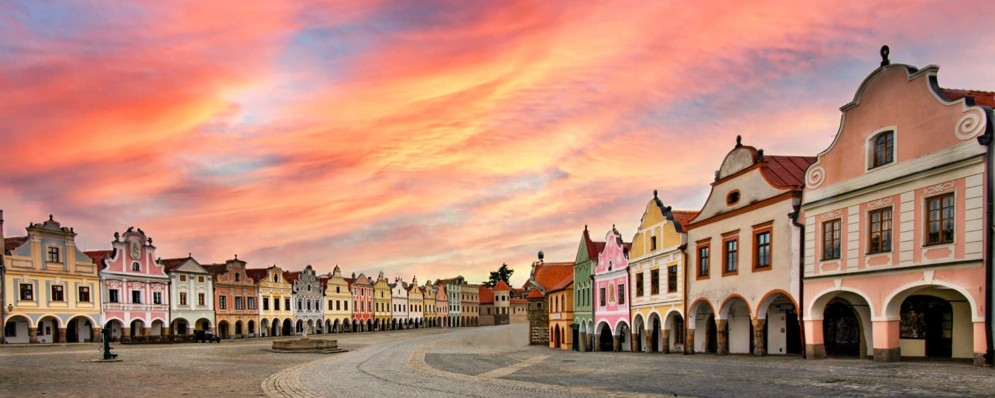 A historical town square with colorful Baroque buildings under a vibrant sunset sky.