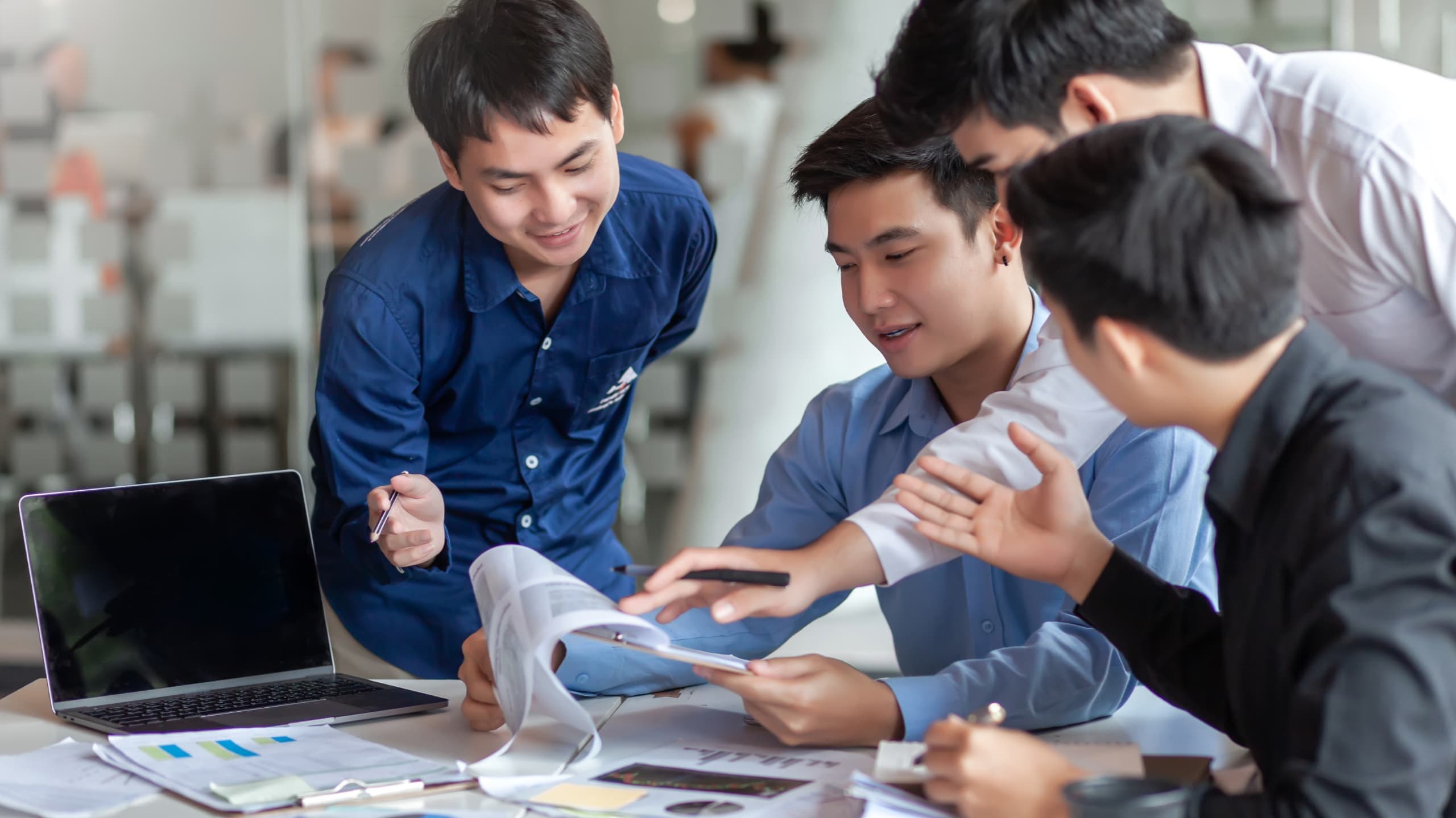 A group of five people having a collaborative discussion around a table in an office setting.