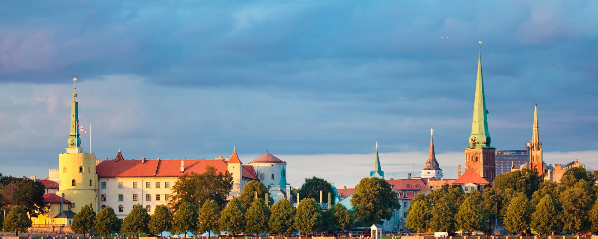 Cityscape with historic buildings, including a tower and spires, against a cloud-filled sky at sunset or sunrise.