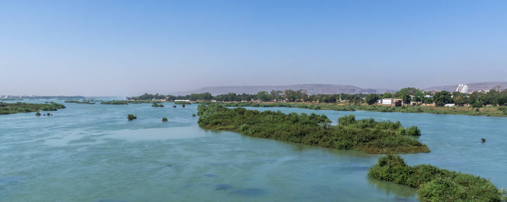 A wide river with green islands and distant hills under a clear blue sky.