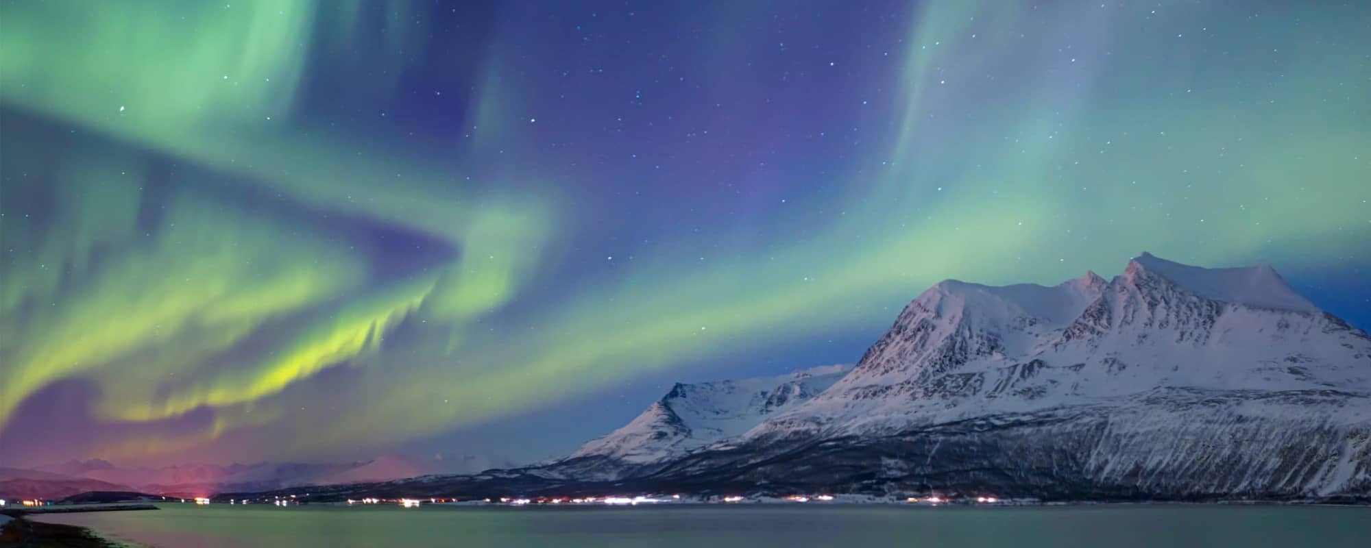 Northern Lights over snow-covered mountains by a calm body of water.