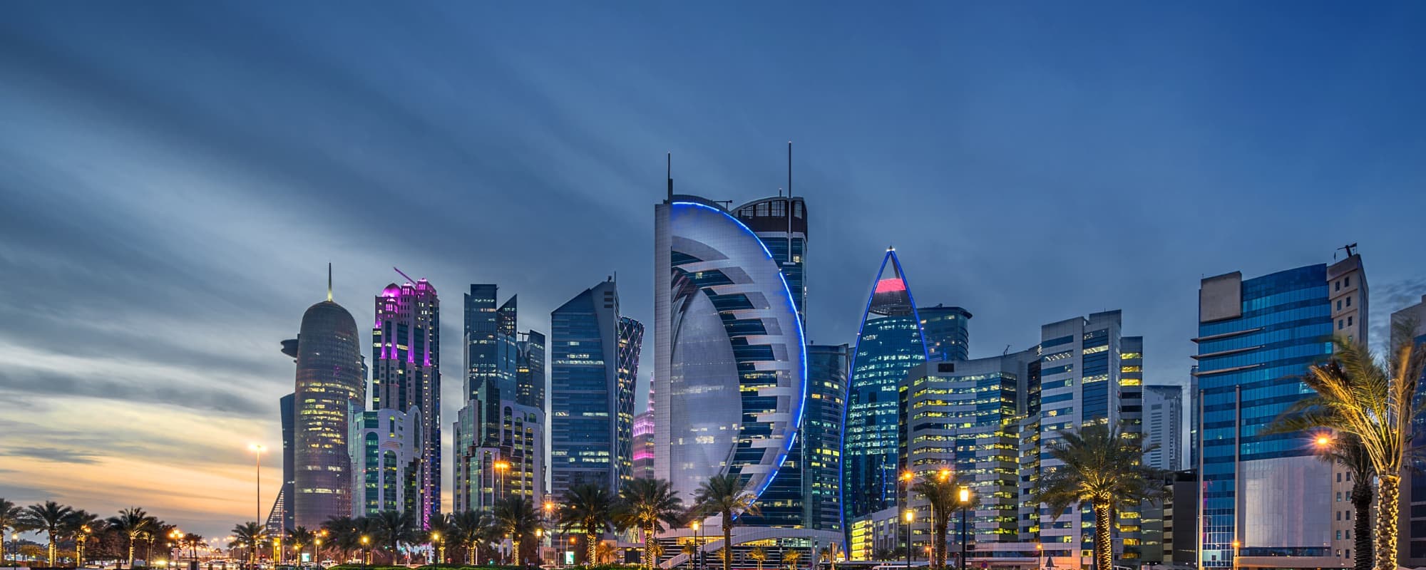 City skyline with modern skyscrapers illuminated at dusk, featuring colorful neon lights.