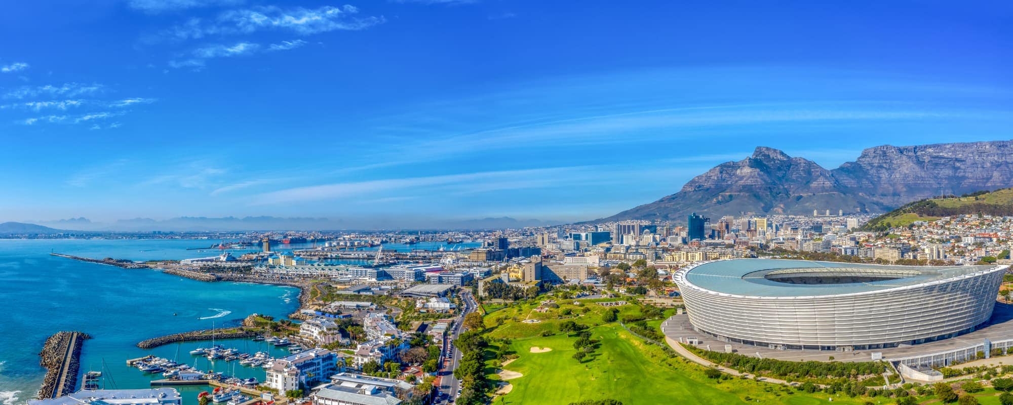 Panoramic view of Cape Town with a large stadium, marina, cityscape, and Table Mountain.