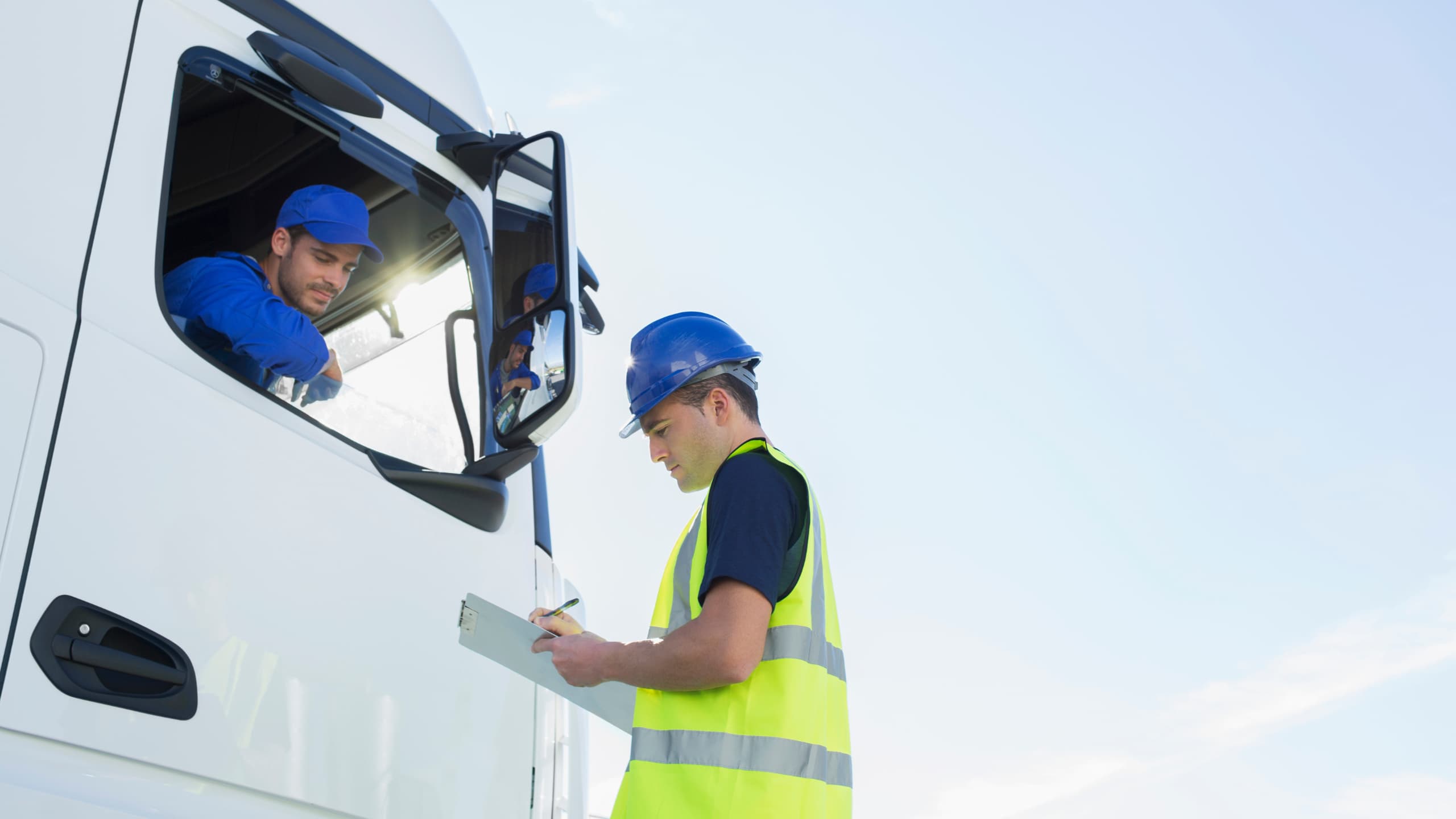 JAS Sweden logistics worker in a high-visibility vest reviewing documents with a driver seated in a commercial truck during a daytime pre-departure inspection.