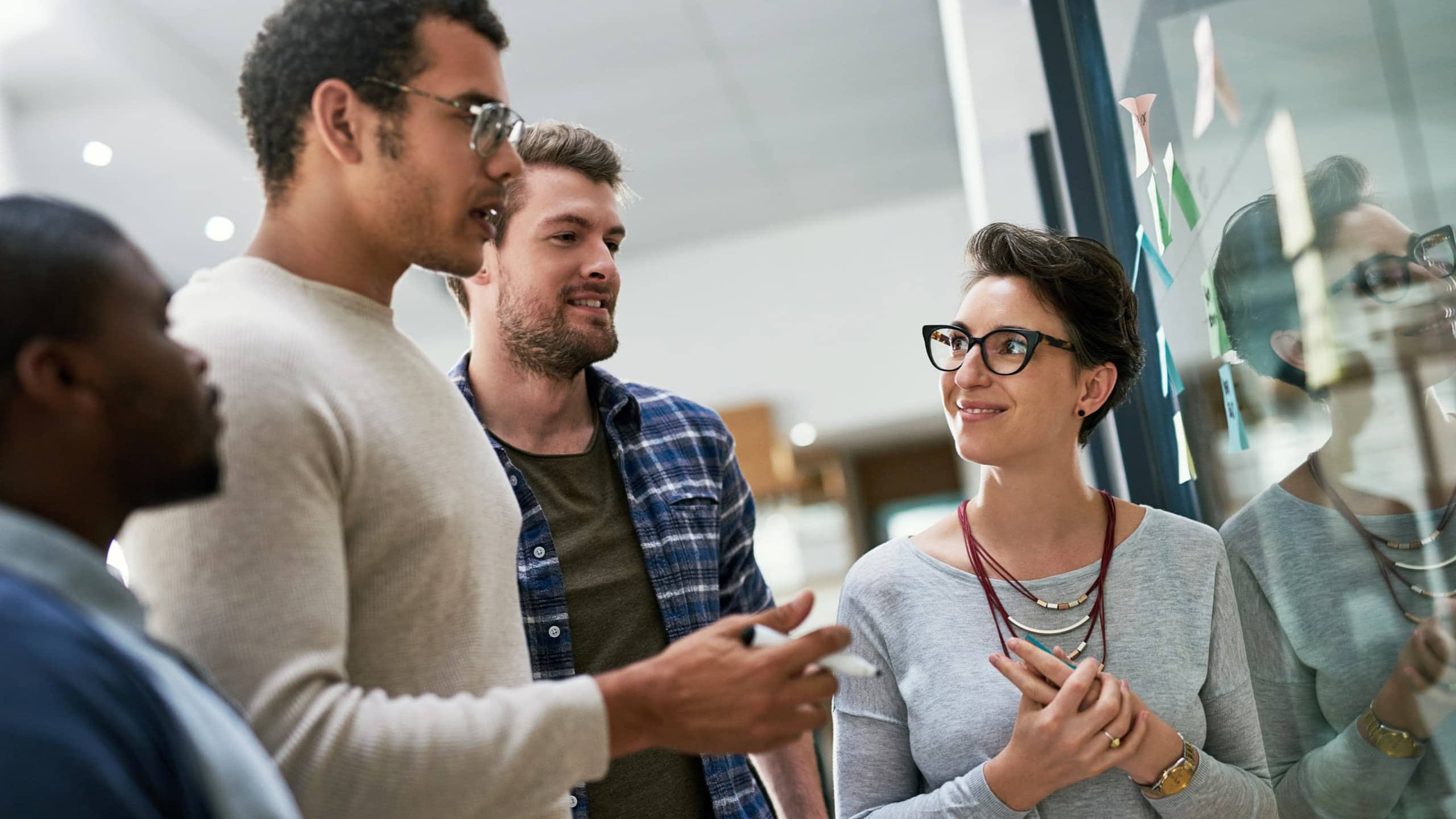 Four people discussing in front of a glass board with sticky notes.