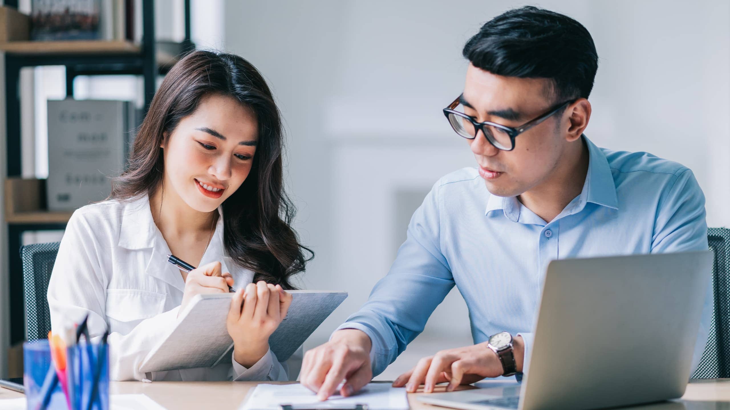 Two people collaborating in an office, with a laptop and documents on the table.