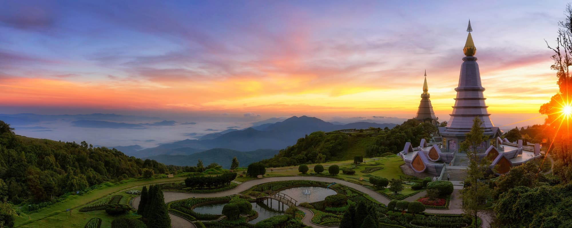 Sunset view of two pagodas on a hill with a landscaped garden and distant mountains.