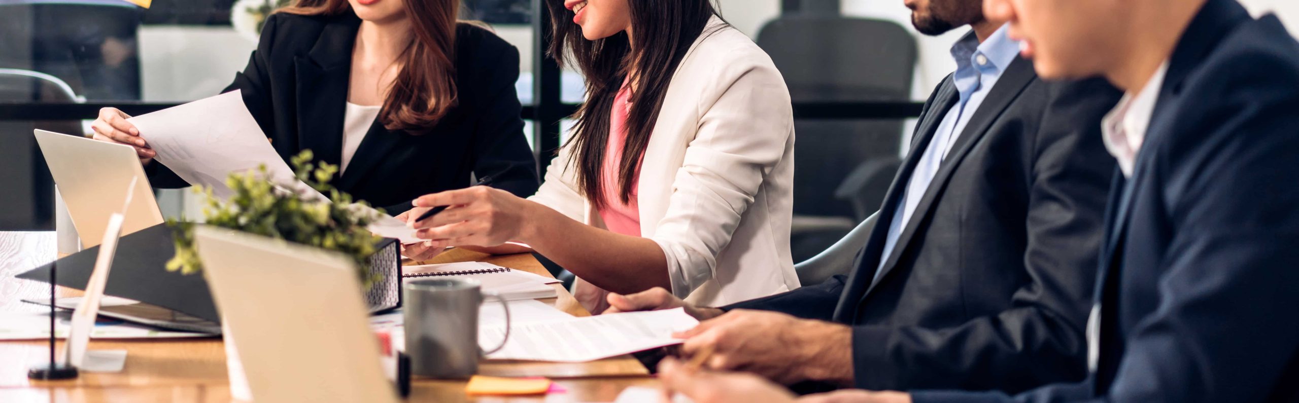 A group of four business professionals in a meeting, with papers and laptops on a table.